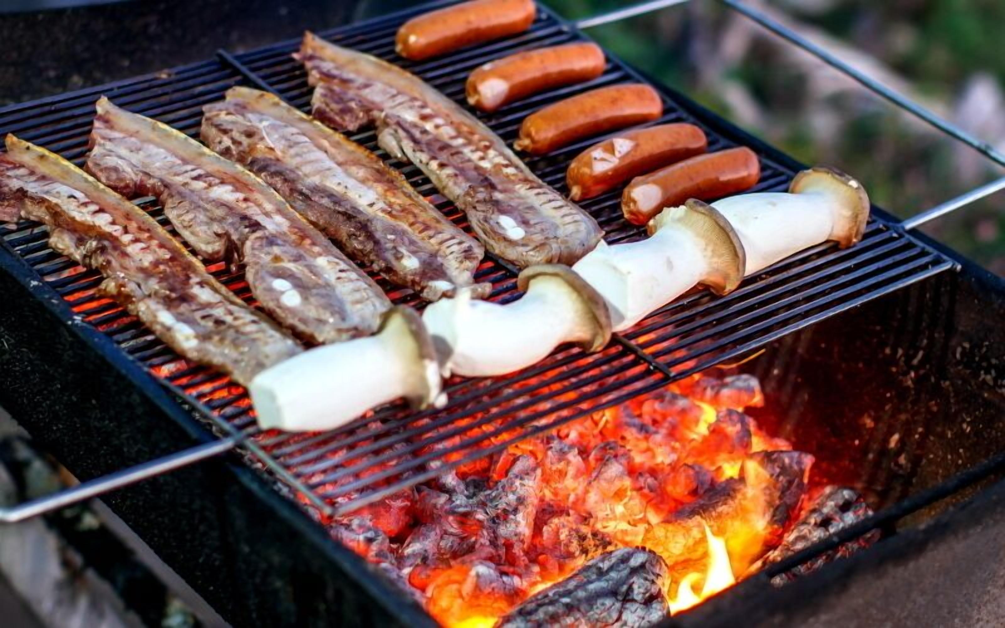 A grill with various meats and mushrooms being cooked over an open flame.