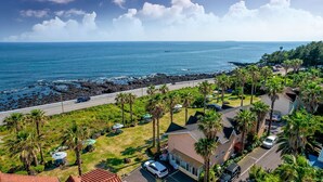 A coastal residential area with a road, parked cars, and a view of the ocean. - Jeju Bada Walking Pension (Seogwipo)