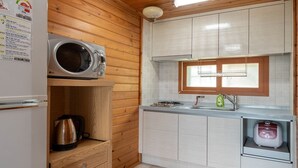 A compact kitchen with wooden walls, a white refrigerator, a microwave, a kettle, and a small sink. - Jeju Bada Walking Pension (Seogwipo)