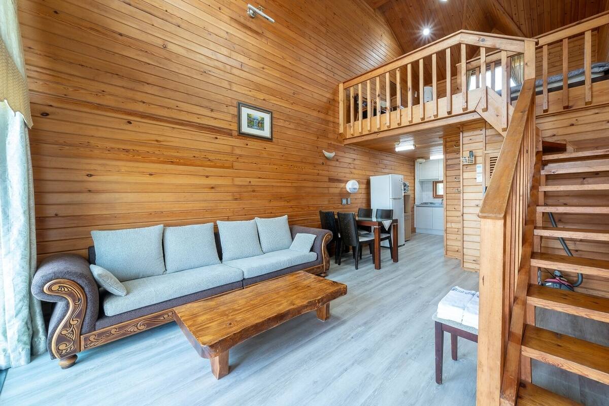 A wooden interior with a sofa, dining table, and staircase.