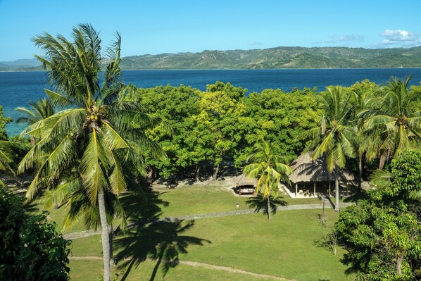 A tropical resort with palm trees, a thatched-roof hut, and a view of the sea.