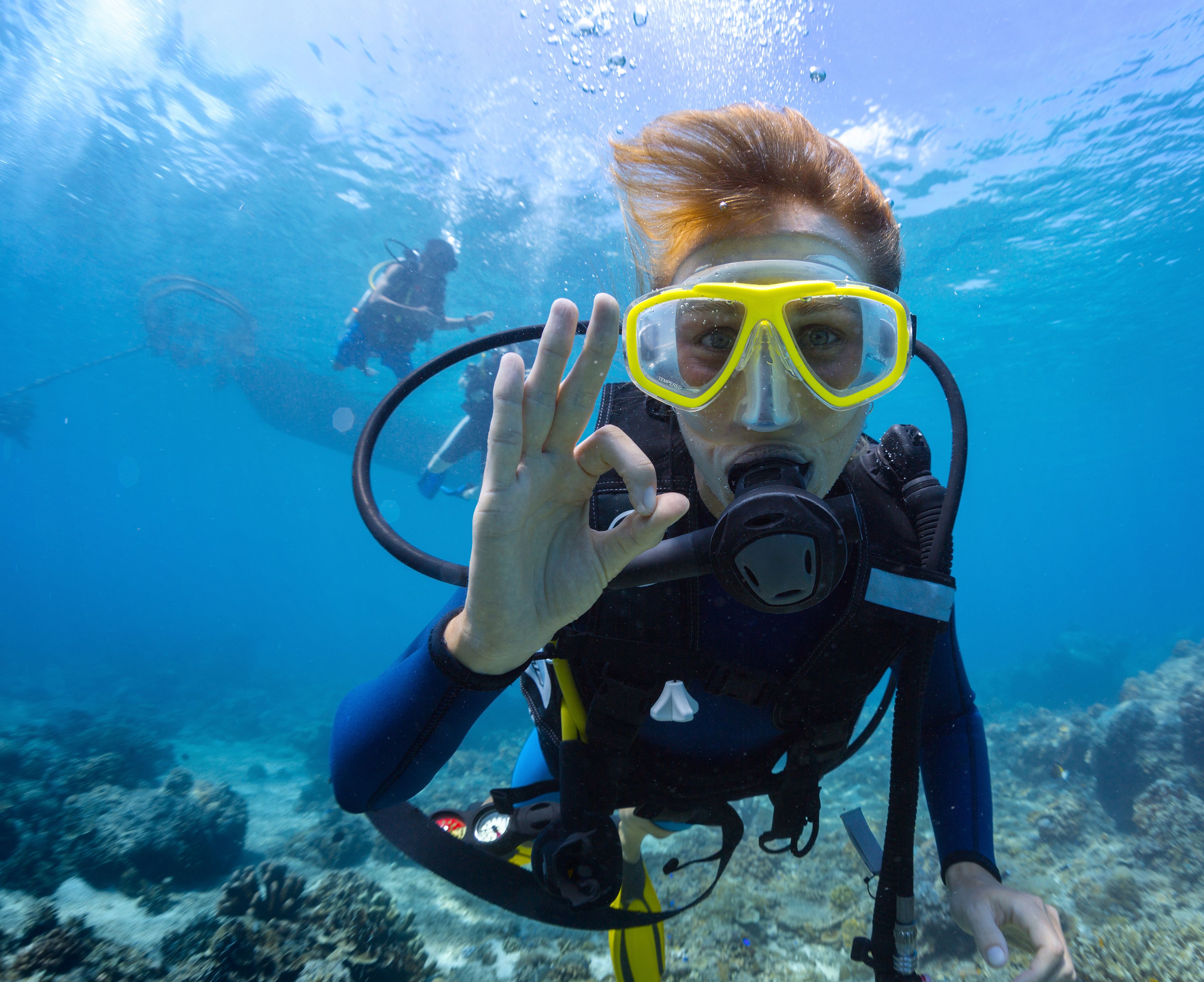 A diver underwater with a scuba mask and fins, surrounded by clear blue water and marine life.
