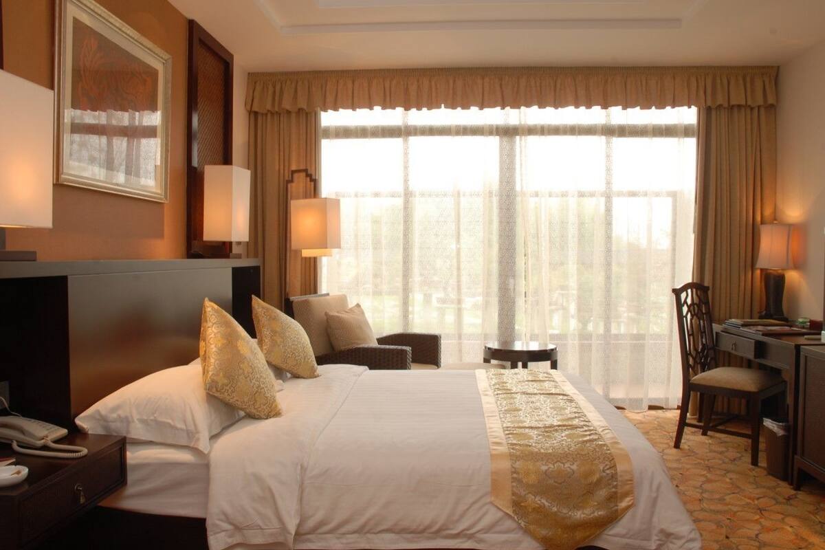 Habitación de hotel con una cama grande, un escritorio, una silla y vistas al exterior a través de un ventanal amplio.