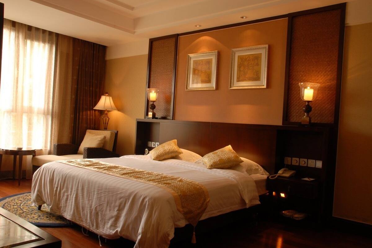 Habitación de hotel con una cama grande, dos lámparas de noche, una mesita de noche con teléfono y un cuadro en la pared.