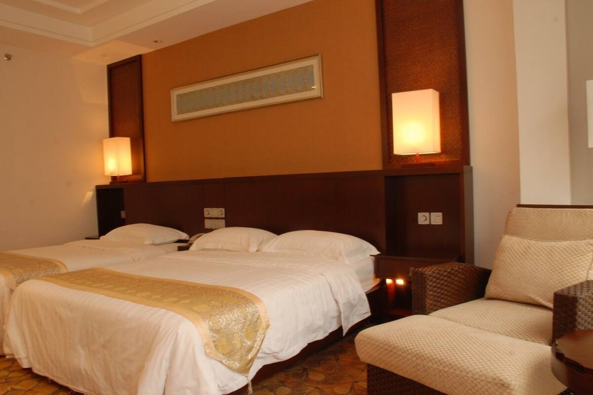 Una habitación de hotel con dos camas, un sofá y una mesita de noche con l ámpara.