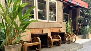 A restaurant with outdoor seating, including wooden tables and chairs, and large potted plants. - 09 Hostel (Chiang Mai)