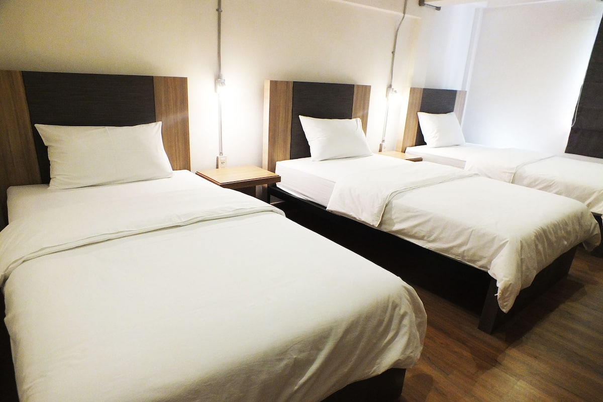 A hotel room with three single beds, each with a wooden headboard and white bedding.