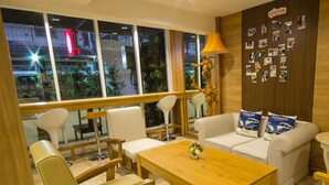 A modern hotel room with a wooden dining table, white sofas, and a large window offering a city view. - 09 Hostel (Chiang Mai)