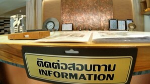 A reception desk with a sign that reads "INFORMATION" in English and another language. There are framed certificates or awards on the wall behind the desk. - 09 Hostel (Chiang Mai)