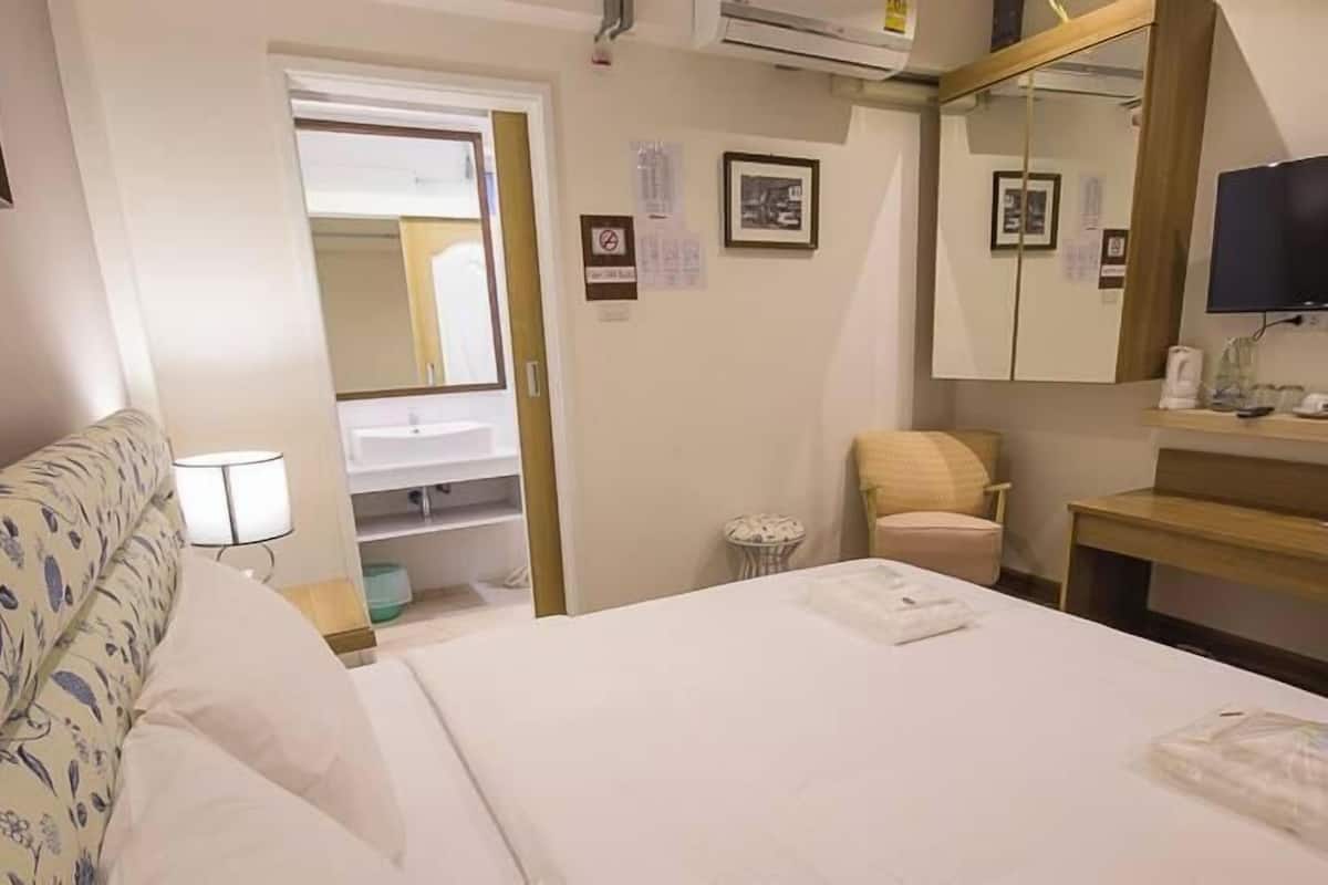A hotel room with a bed, a chair, a small table, a mirror, a television, and a bathroom visible through an open door.