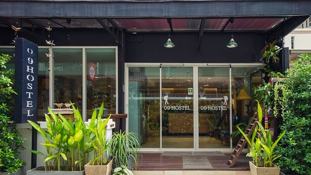 A modern hostel with a glass facade, labeled "09 HOSTEL," and potted plants at the entrance. - 09 Hostel (Chiang Mai)