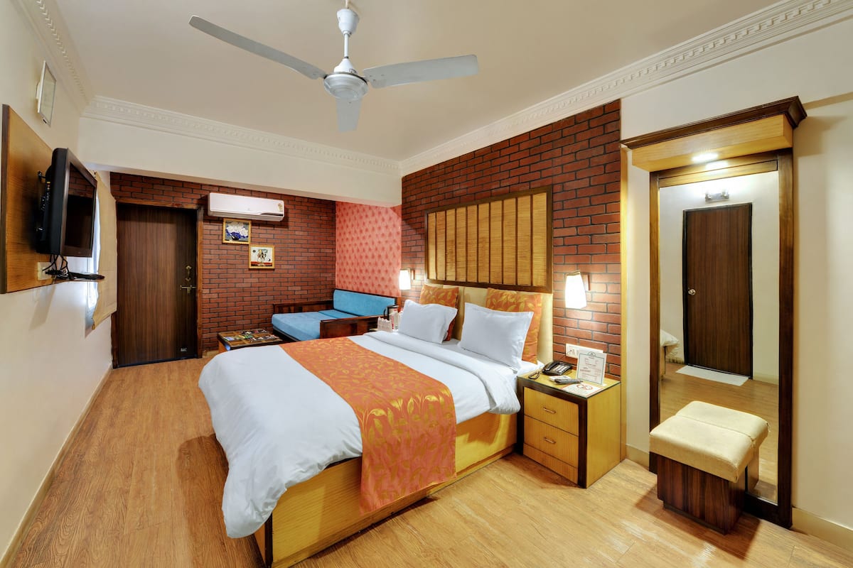 Una habitación de hotel con una cama grande, un banco de madera, un televisor, un escritorio y un armario.