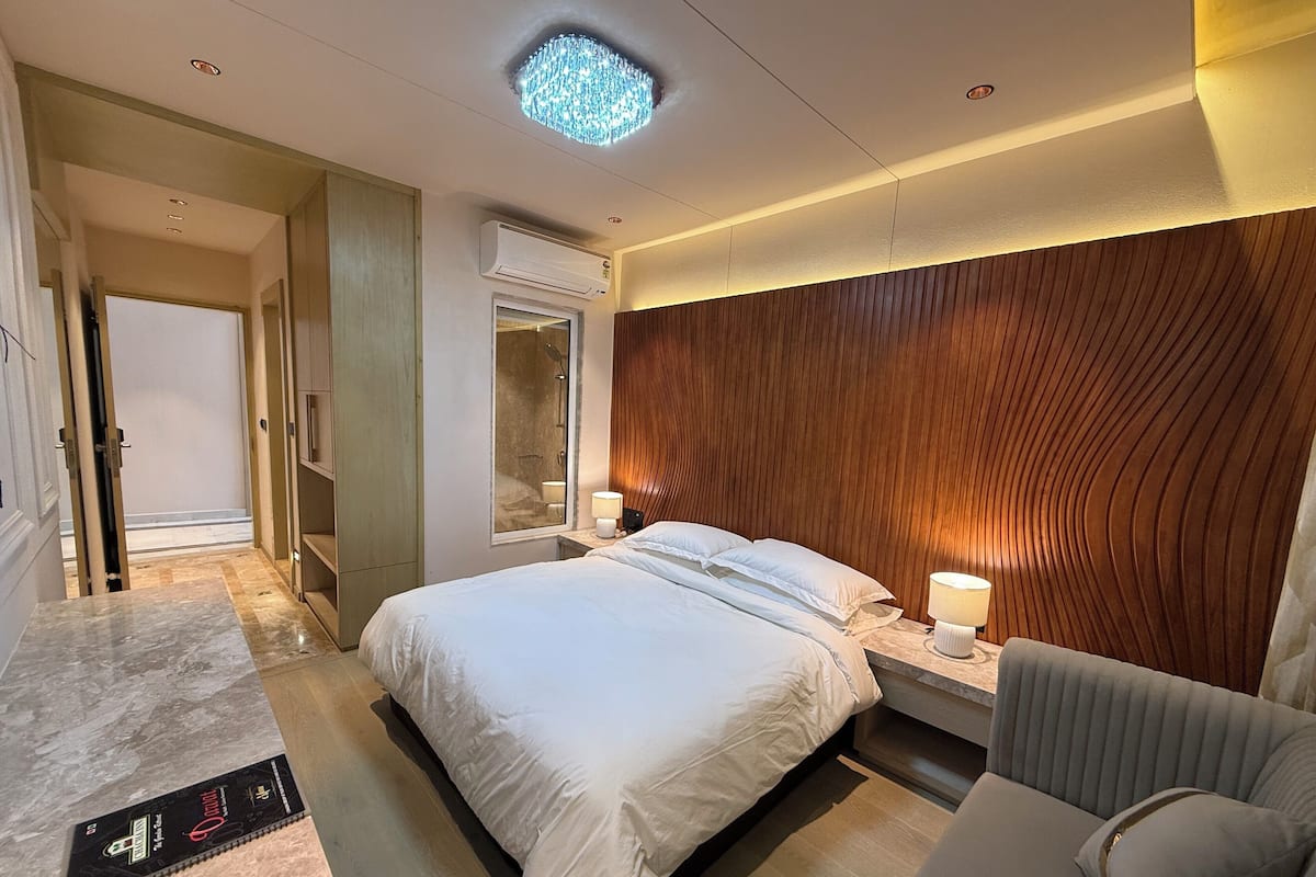 Habitación de hotel con una cama grande, lámparas de noche, un cabecero de madera, un baño con espejo y un equipo de aire acondicionado.