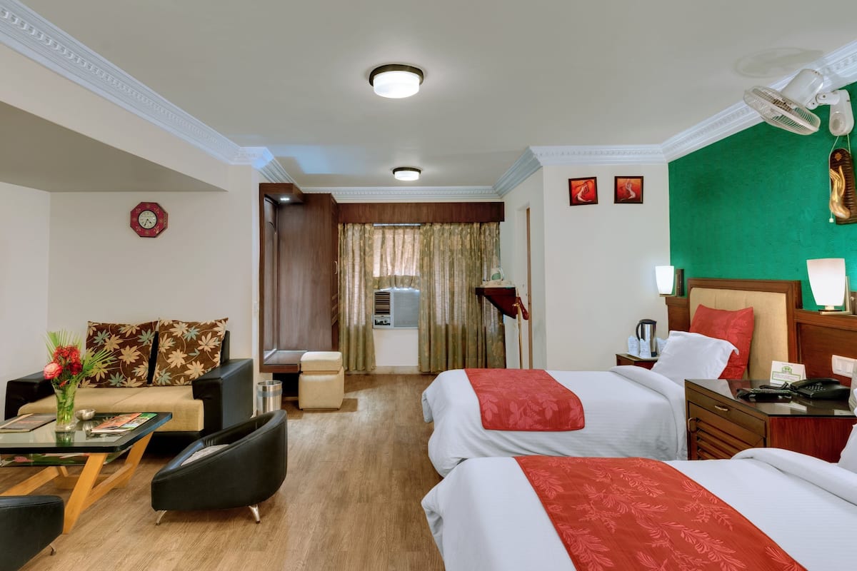 Habitación de hotel con dos camas, un escritorio con silla, televisor, reloj y ventana con cortinas.