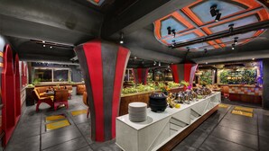 Un bar moderno con una barra alargada, detalles en rojo y una variedad de plantas.