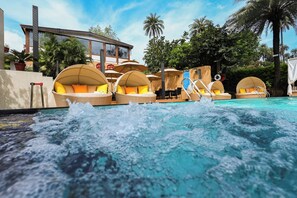 A pool area with lounge chairs and umbrellas, a building with large windows, and palm trees in the background. - Chacha Inn (Abu Road)