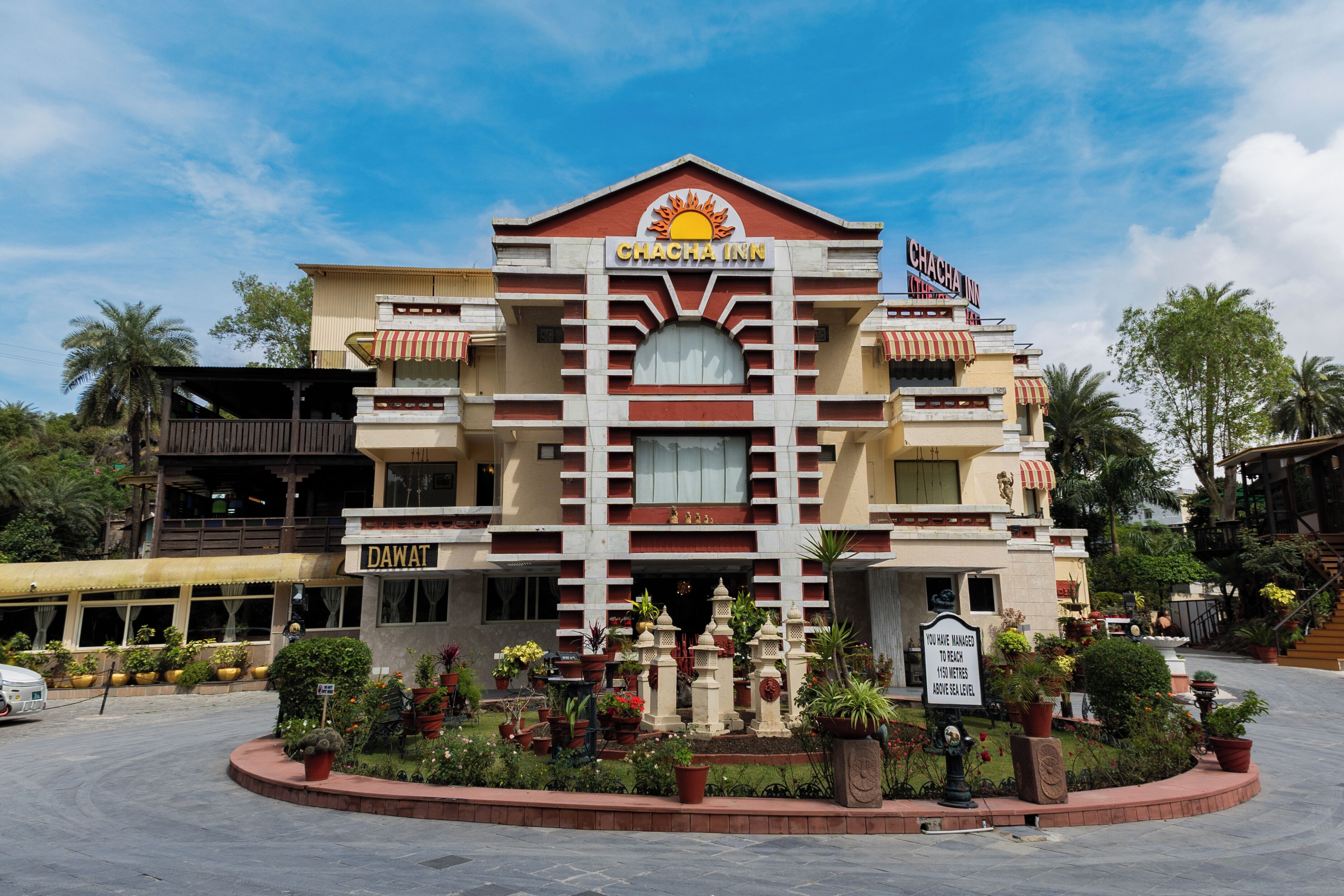 Um hotel com entrada central, várias varandas e um jardim bem cuidado.