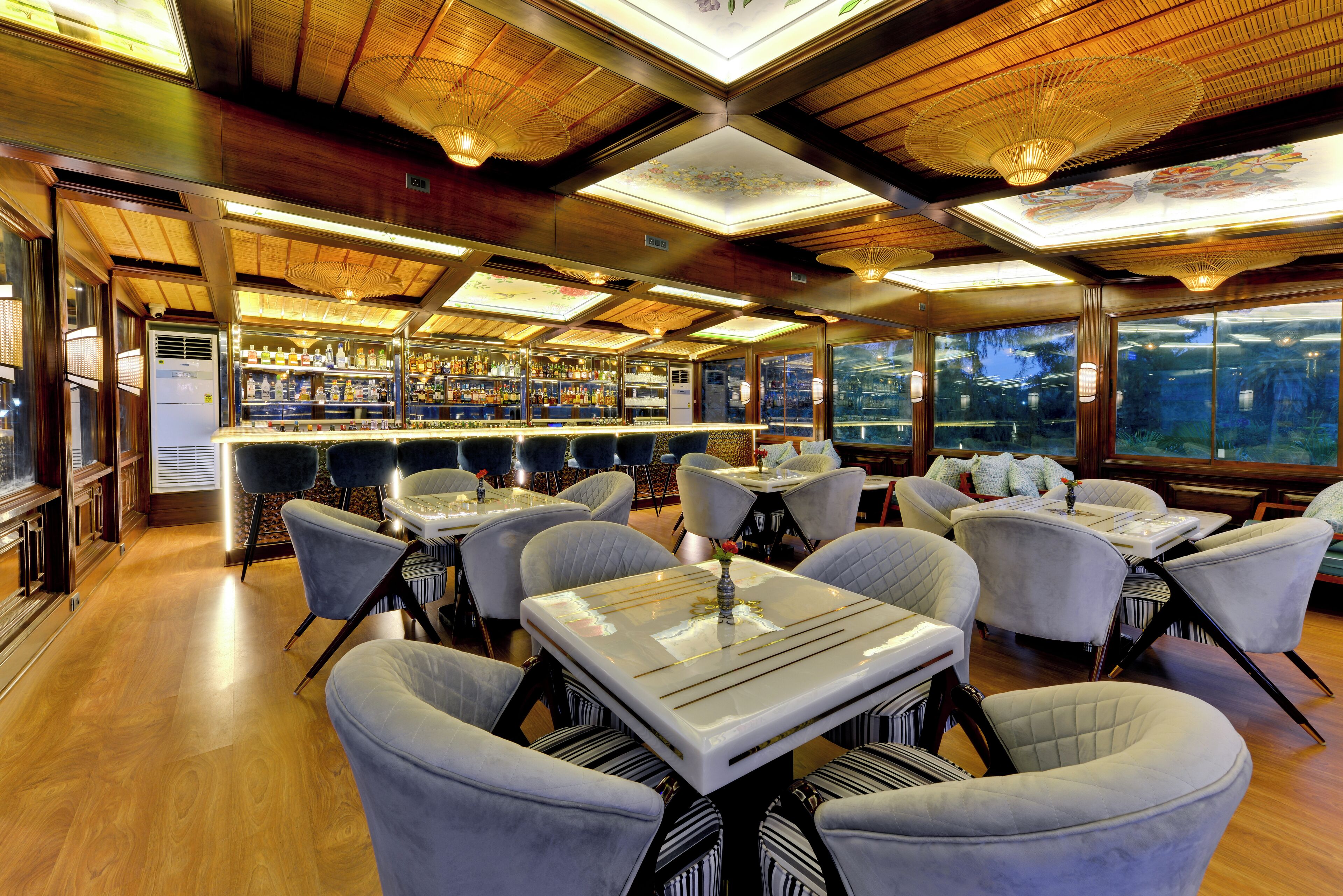 A restaurant with a bar area, multiple tables and chairs, and large windows offering a view of the city.
