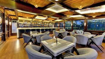 A restaurant with a bar area, multiple tables and chairs, and large windows offering a view of the city.