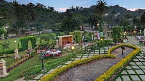 Un jardín con un sendero pavimentado, zonas de estar y una pequeña construcción con techo.