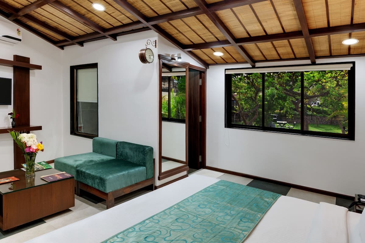 Una habitación moderna con un sofá verde, un escritorio de madera, un televisor y un ventanal con vistas a zonas verdes.
