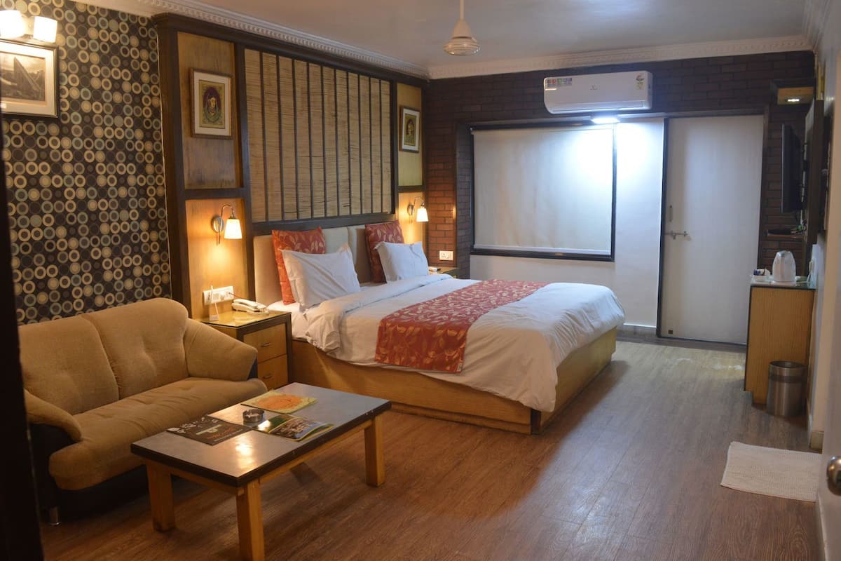 Habitación de hotel con cama, sofá, mesita de noche, lámpara, aire acondicionado instalado en la pared y ventana.