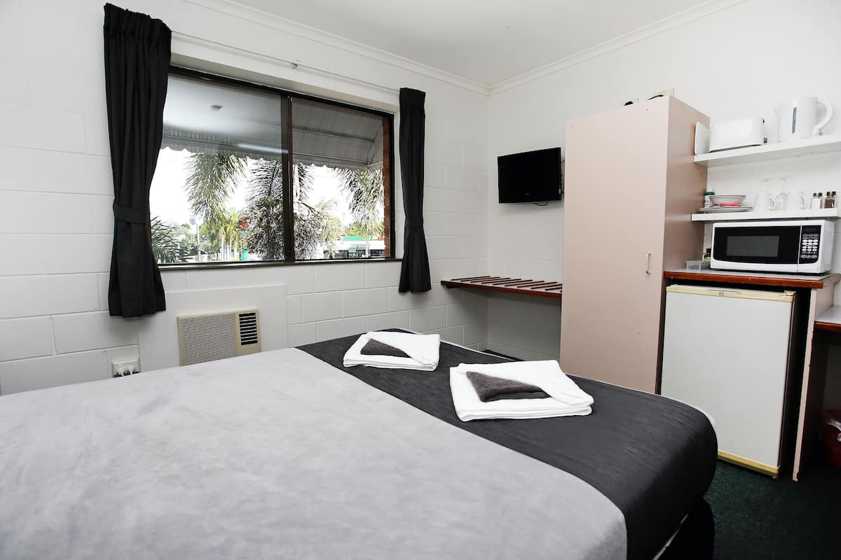Hotellihuone, jossa on sänky, pieni keittonurkkaus, televisio ja ikkuna, jossa on verhot.