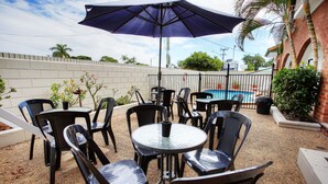Une terrasse extérieure avec des tables et des chaises rondes, une piscine en arrière-plan et un mur en briques.