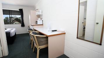 A compact room with a bed, a desk with chairs, a microwave, and a mirror.