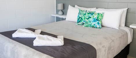 A neatly made bed with white and gray linens, a green and white pillow, and two white towels on the bed.