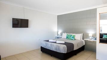 Una habitación de hotel con una cama, un televisor de pantalla plana montado en la pared, una mesita de noche con una lámpara y una ventana con vistas.