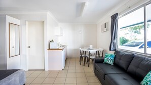 Un espace de vie compact comprenant un coin cuisine, un coin repas et un canapé agrémenté de coussins décoratifs.