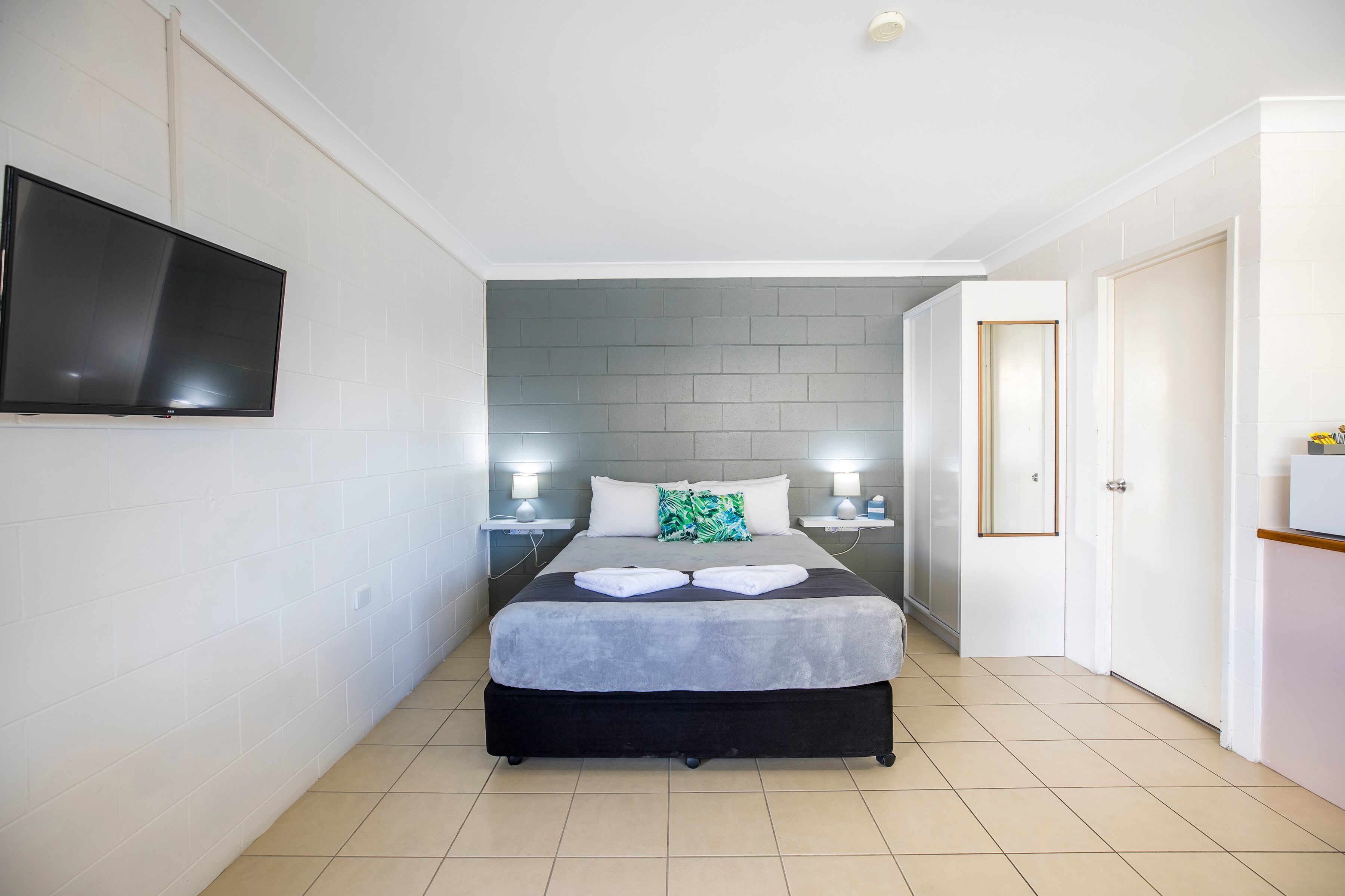 A hotel room with a bed, a flat-screen TV mounted on the wall, and a door leading to another room.