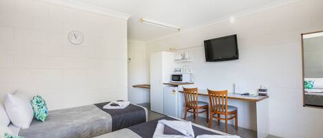 Habitación de hotel con dos camas, un escritorio con silla, microondas y televisión.