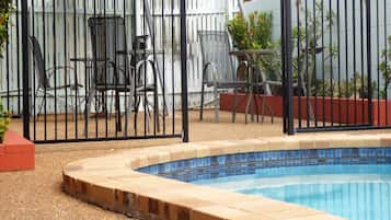 A swimming pool with a tiled edge, surrounded by a fence and chairs.