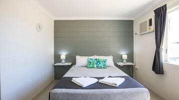 A hotel room with a bed, two bedside tables with lamps, a window with curtains, and a wall clock.