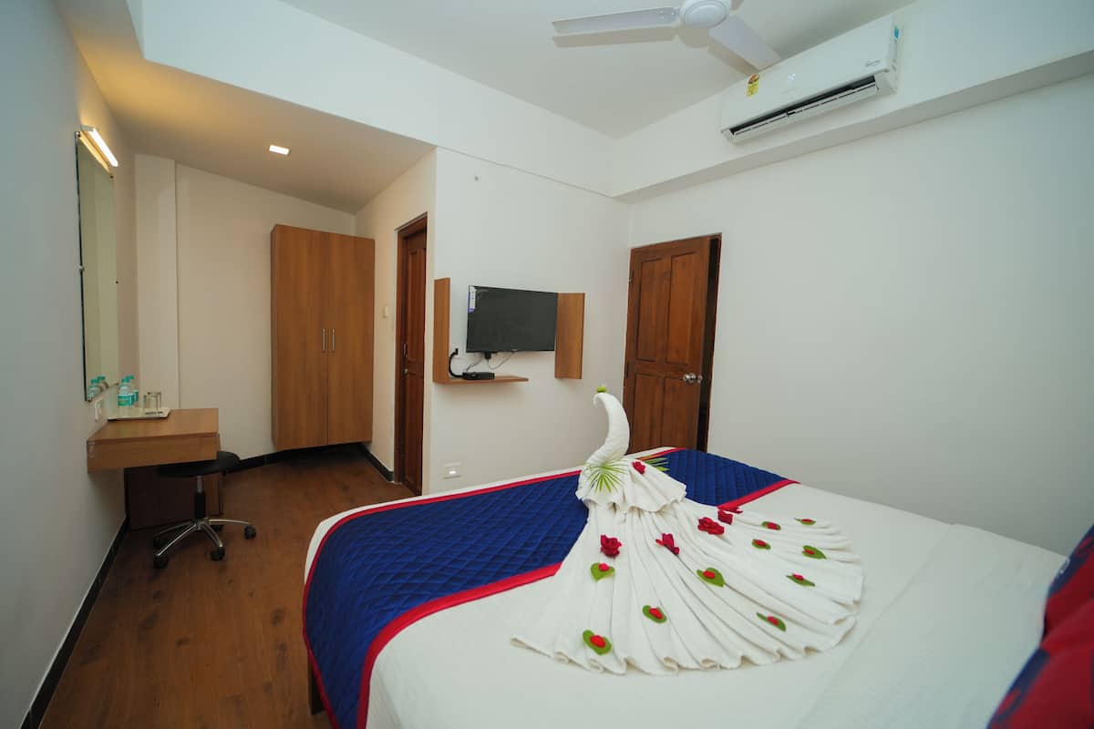 A hotel room with a bed, a desk, a chair, a television, and an air conditioning unit.