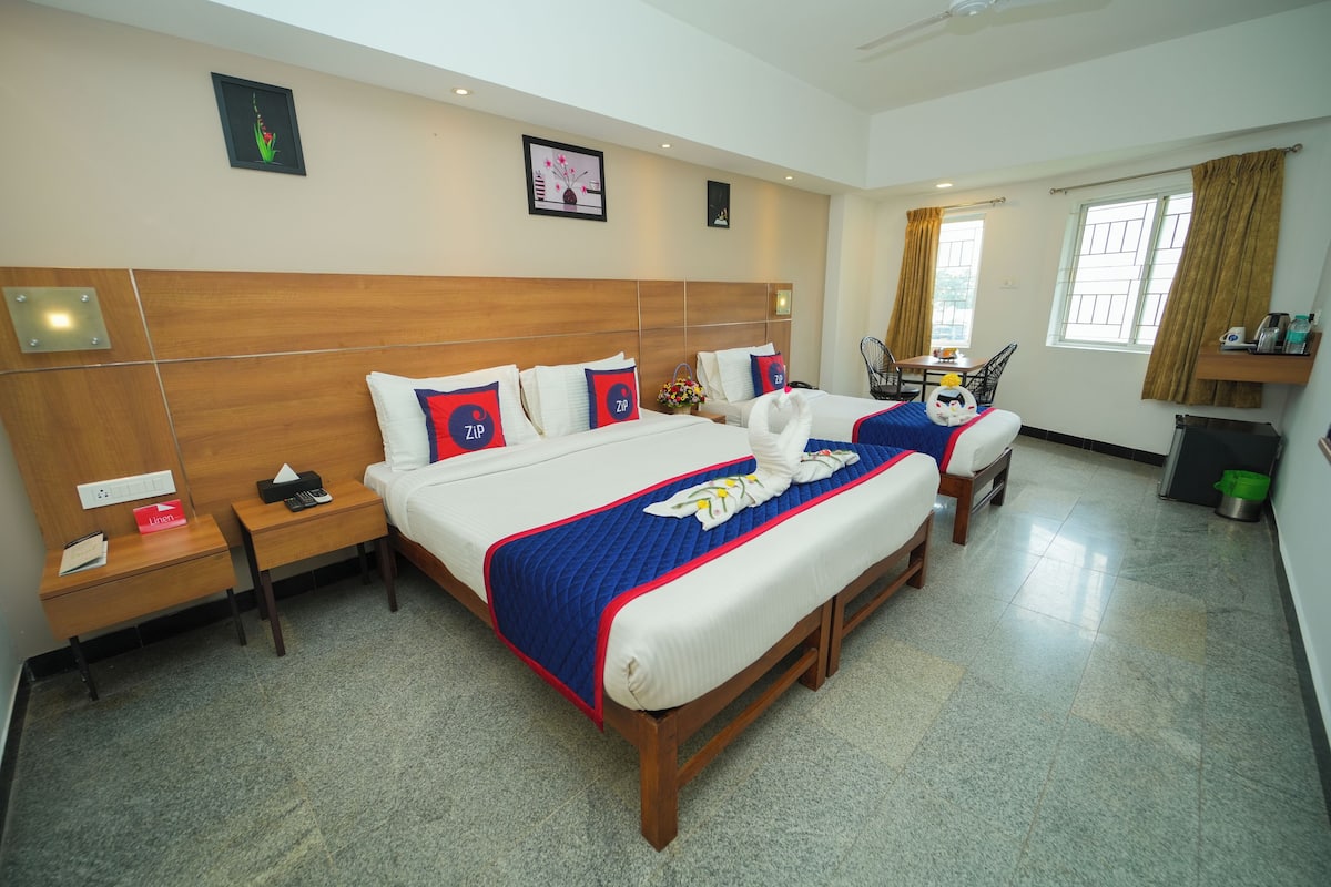A hotel room with two beds, wooden headboards, a small table, and a chair.