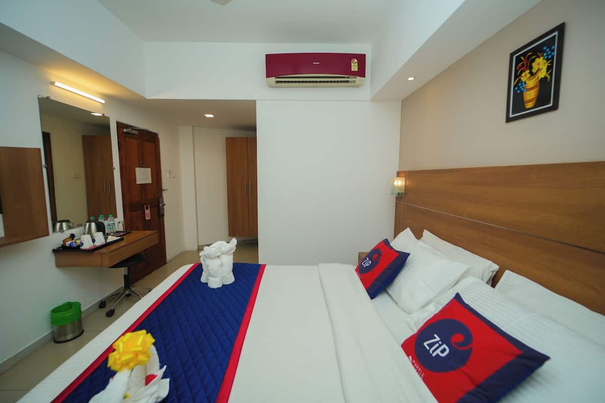 A hotel room with a bed, a desk, a mirror, an air conditioner, and a painting on the wall.