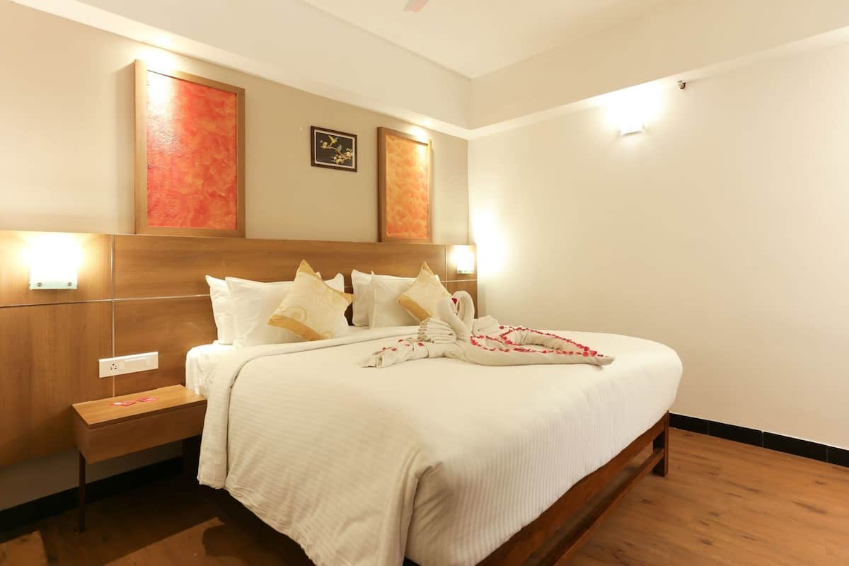 A hotel room with a wooden headboard, a large bed with white bedding, a nightstand, and wall-mounted lights.