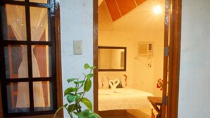 A room with a bed, a potted plant, a mirror, and a window with curtains. - CED Villas (El Nido)