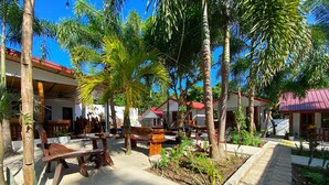 A tropical outdoor seating area with wooden furniture, palm trees, and a paved walkway. - CED Villas (El Nido)