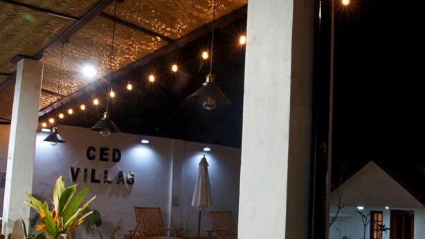A cozy indoor seating area with wooden chairs and tables, a hanging light fixture, and a wall with 'CED VILLAS' signage. - CED Villas (El Nido)