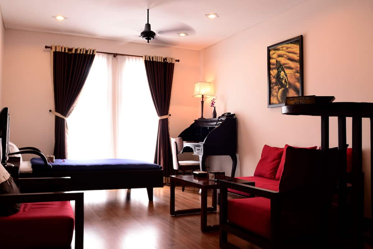 A hotel room with a bed, a desk, a chair, a red sofa, and a painting on the wall.