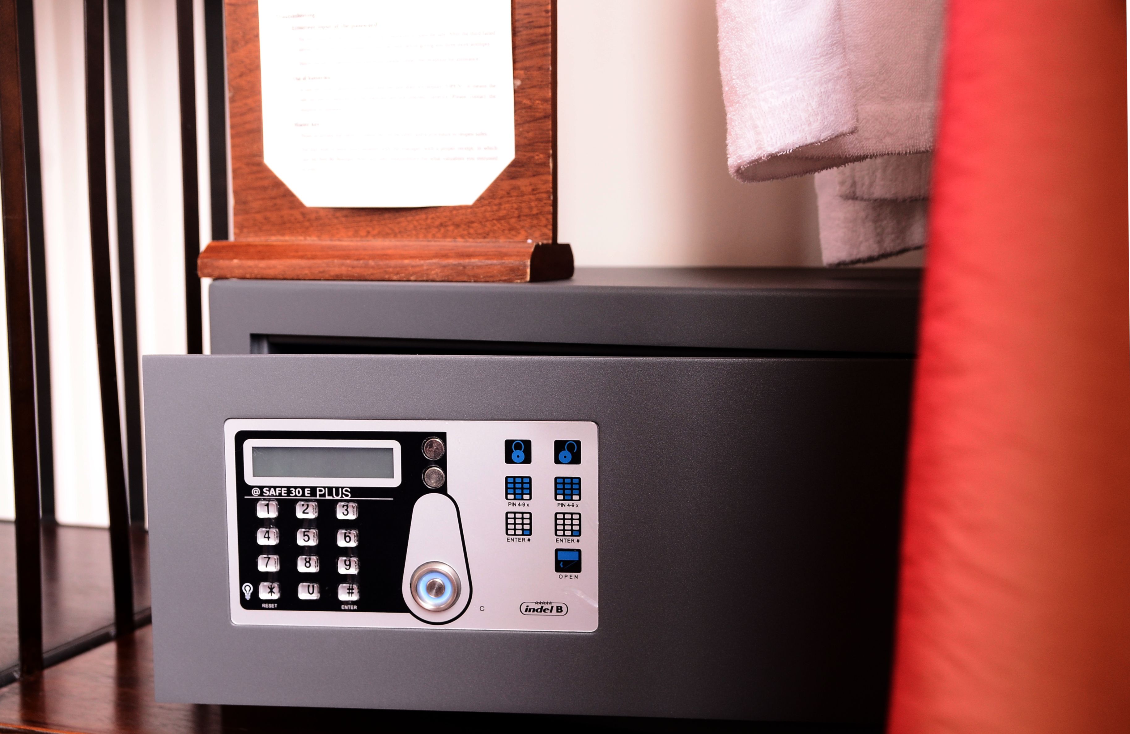 A safe with a keypad and a small screen, placed on a wooden surface with a towel nearby.