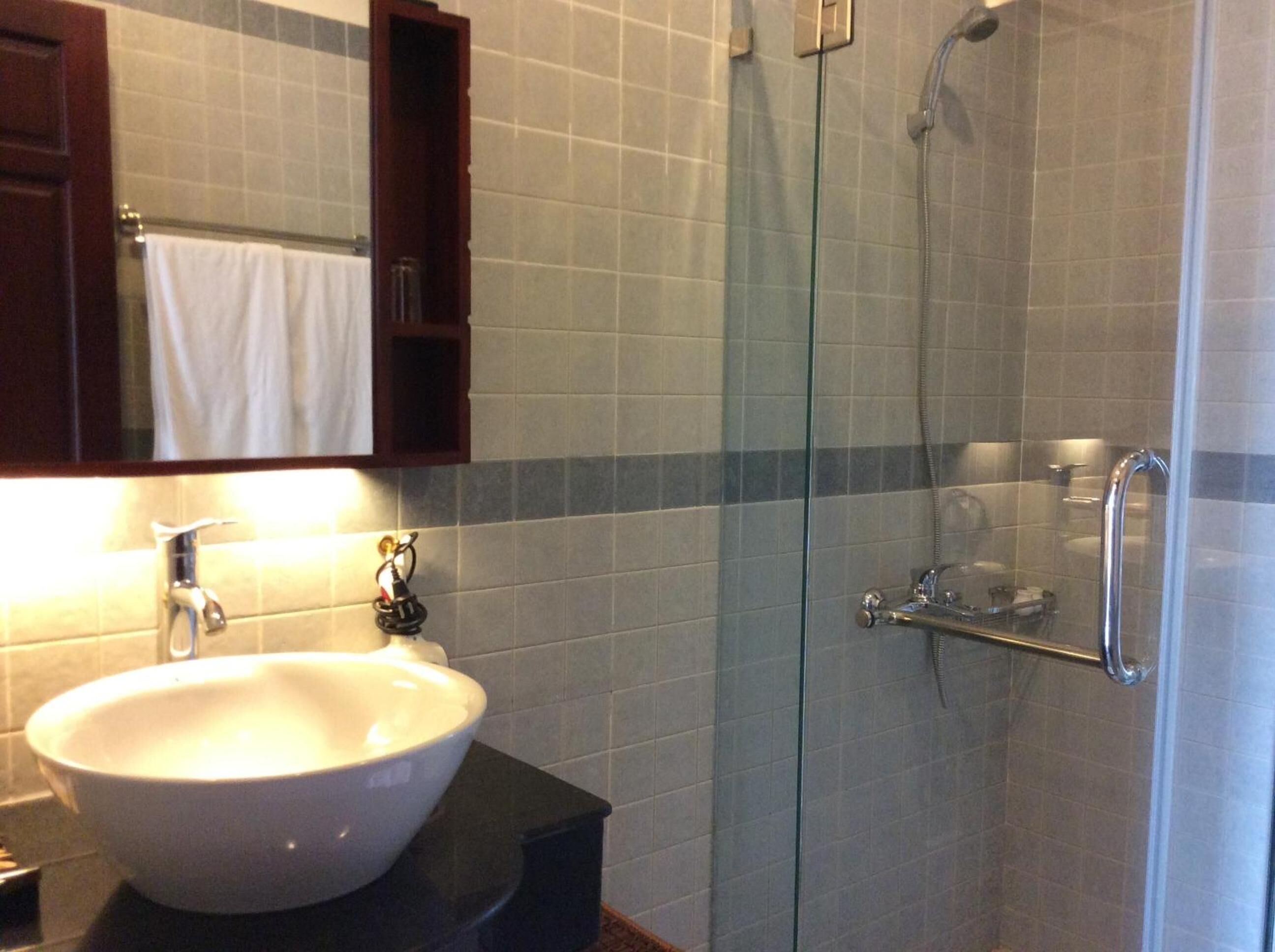 Un baño con un lavamanos blanco, cabina de ducha con mampara de vidrio y un espejo con una toalla colgando.