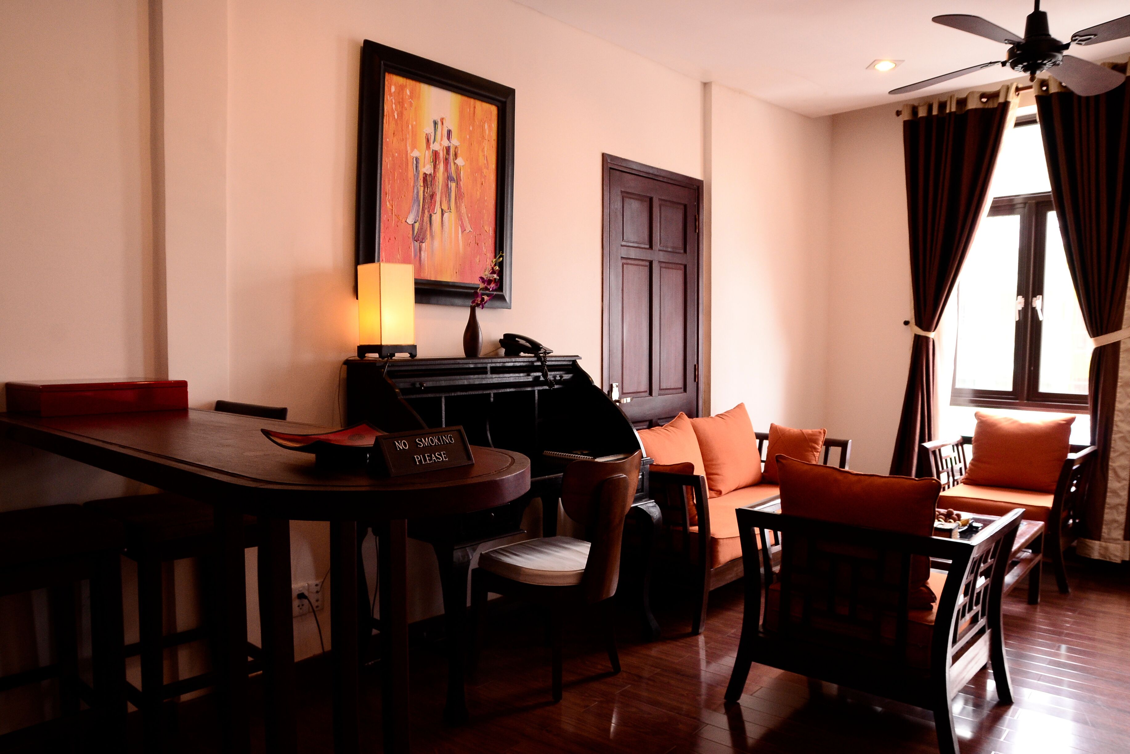 A hotel room with a dining area, a sofa with orange cushions, a painting on the wall, and a door with a window.