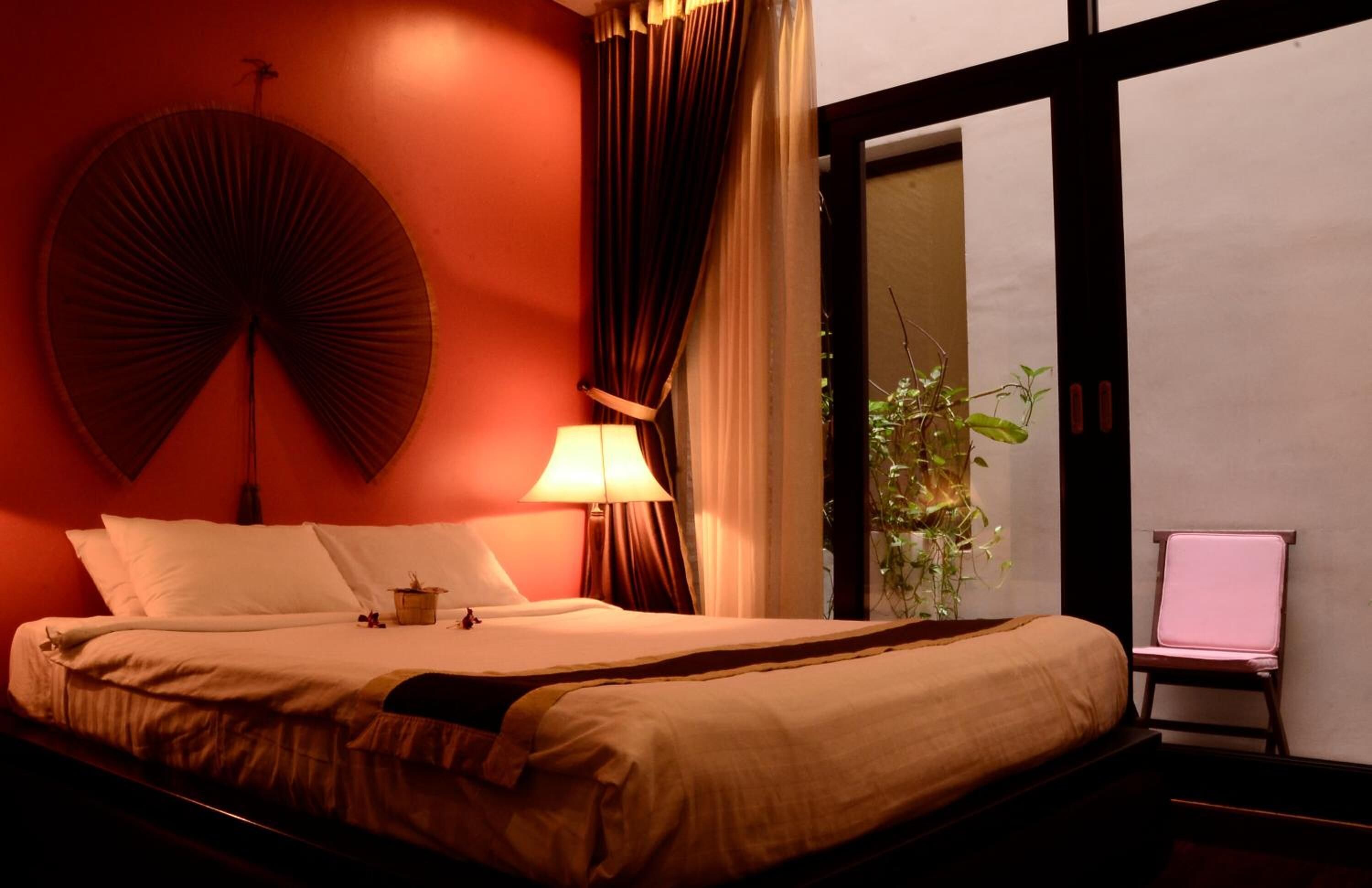 A hotel room with a bed, a lamp, a chair, and a window with curtains.