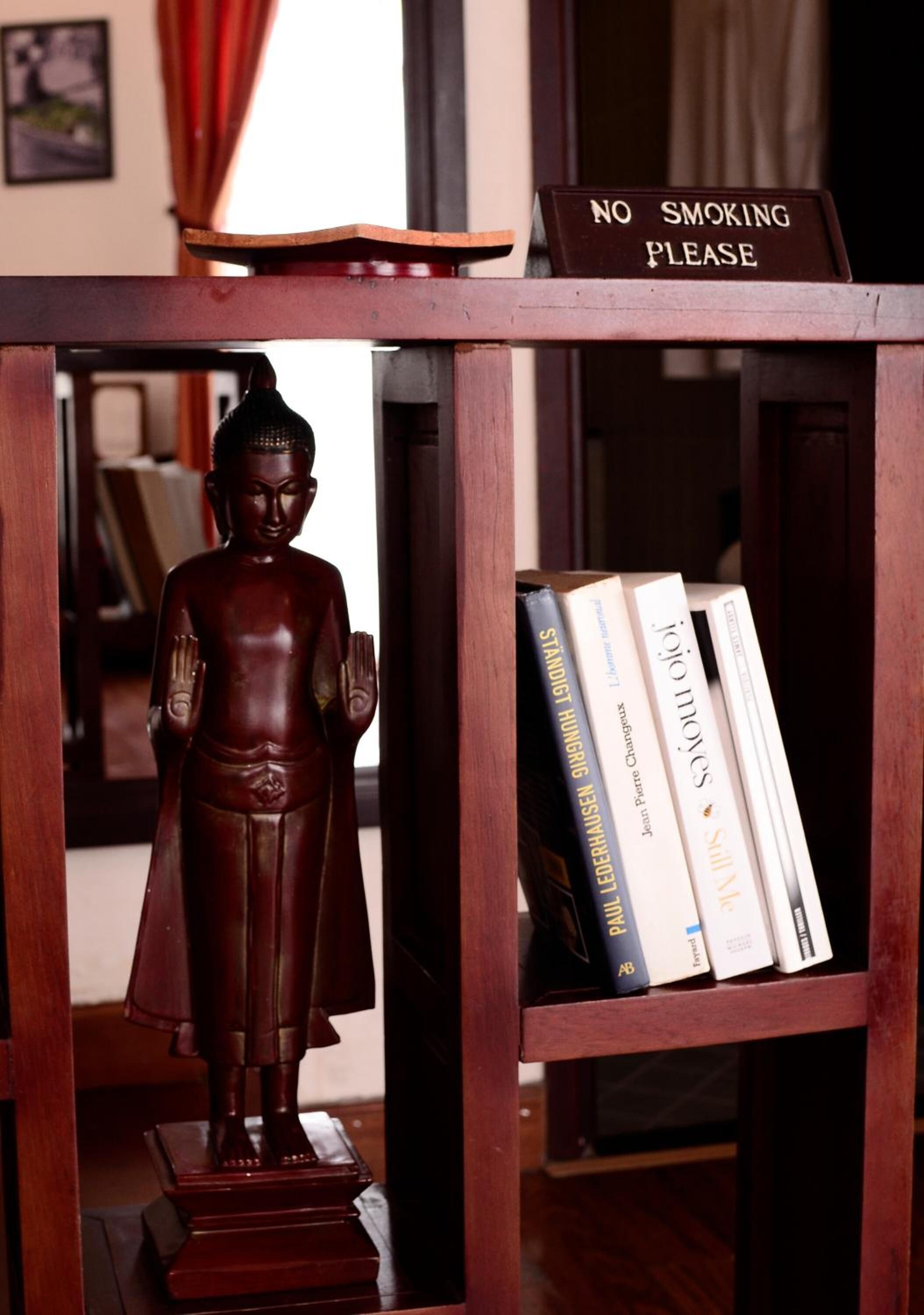 A wooden shelf with a Buddha statue, books, and a 'No Smoking' sign.