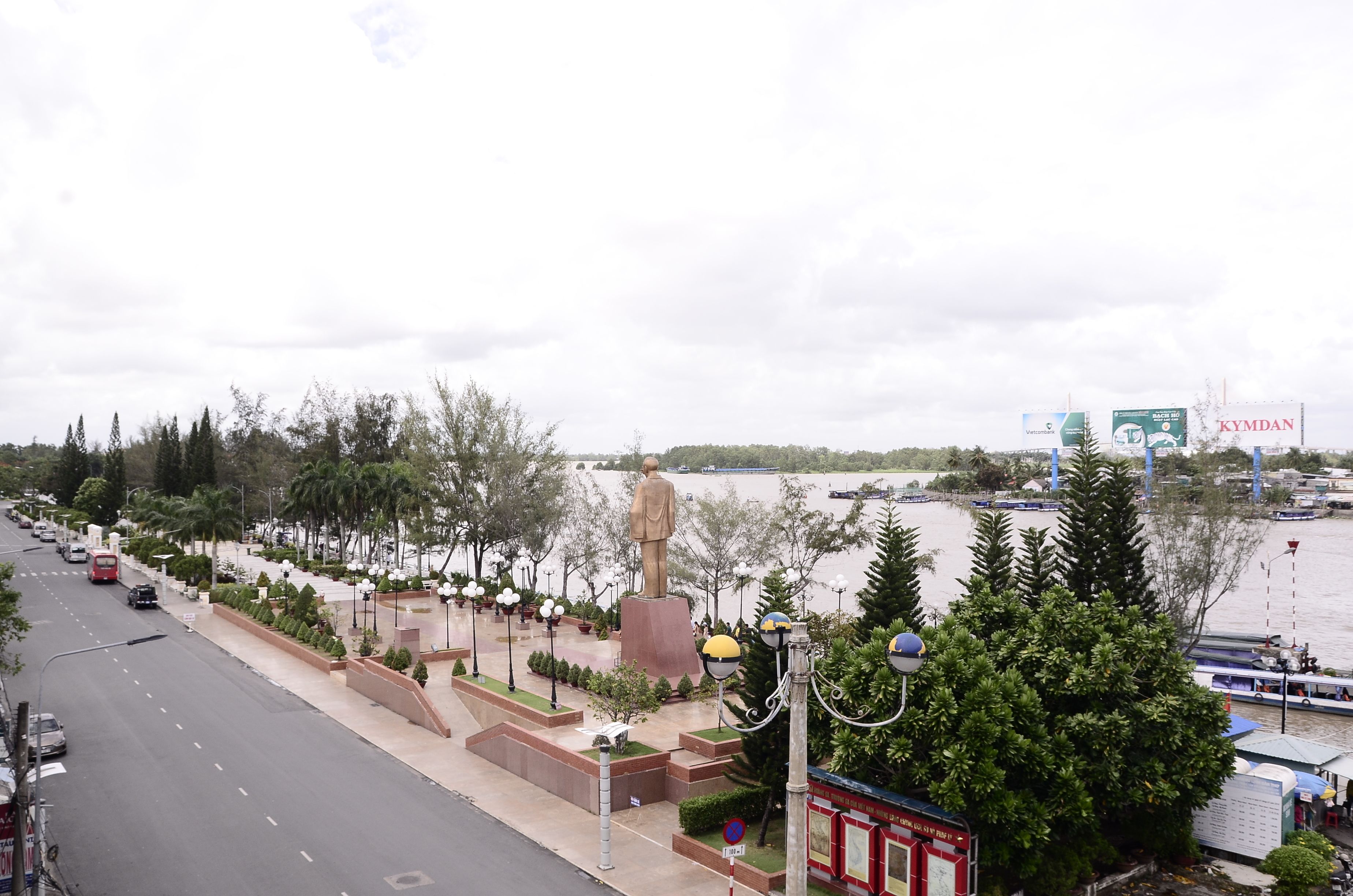 Un paseo ribereño con una estatua, bancos y farolas.